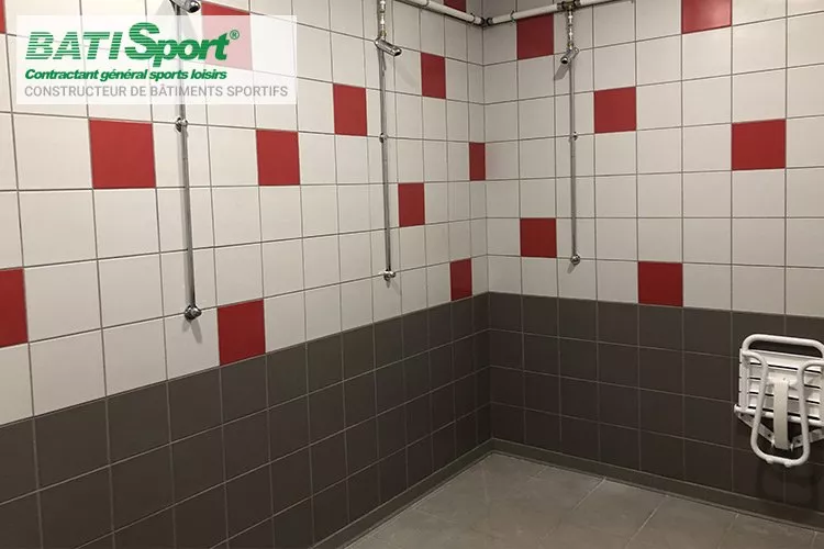 Douches des vestiaires avec carrelage blanc rouge et gris clair.